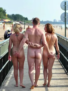 a guy getting a feel of the asses of two nude lady friends as they walk along in public.